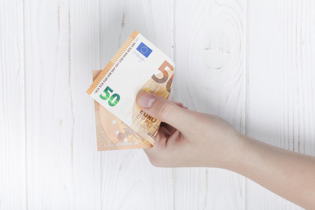 billet de 50 € plié en deux au creux d'une main tendue